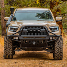 Load image into Gallery viewer, The front end of a Toyota Tacoma featuring an impressive Old Man Emu 2.5 inch Lift Kit for Tacoma (16-23) suspension system and Nitrocharger shocks, resulting in exceptional ground clearance.