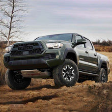 Load image into Gallery viewer, The 2019 Toyota Tacoma, equipped with the OME 2.5 inch Lift Kit for Tacoma (16-23) from Old Man Emu, confidently drives on a dirt road, showcasing its excellent ground clearance.