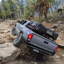 Load image into Gallery viewer, A Toyota Tacoma equipped with an Old Man Emu OME 2.5 inch Lift Kit for Tacoma (16-23) suspension system and Nitrocharger shocks is confidently navigating a rocky trail, effortlessly handling the terrain thanks to its exceptional ground clearance.
