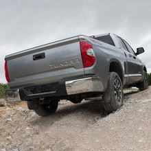 Load image into Gallery viewer, The rear end of a gray Toyota Tundra truck showcasing its off-road performance with the Old Man Emu OME BP-51 2.5 - 3 inch Lift Kit for Tundra (07-21) on a dirt road.
