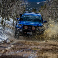 Load image into Gallery viewer, A blue Toyota Tacoma equipped with an Old Man Emu OME BP-51 2-3 inch Lift Kit for Tacoma (05-23) suspension system and shock absorbers is smoothly driving down a dirt road, showcasing its exceptional adjustable damping feature.