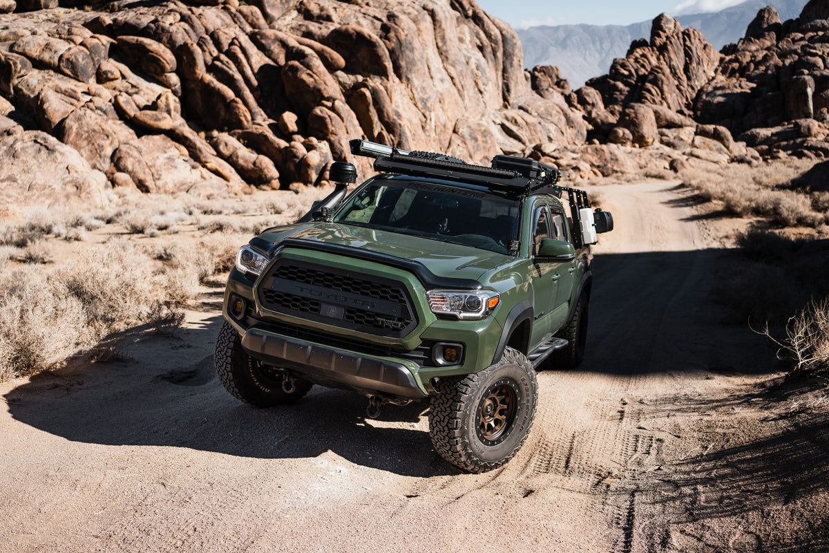 Green off-road pickup truck with roof rack and all-terrain tires on a rocky desert trail