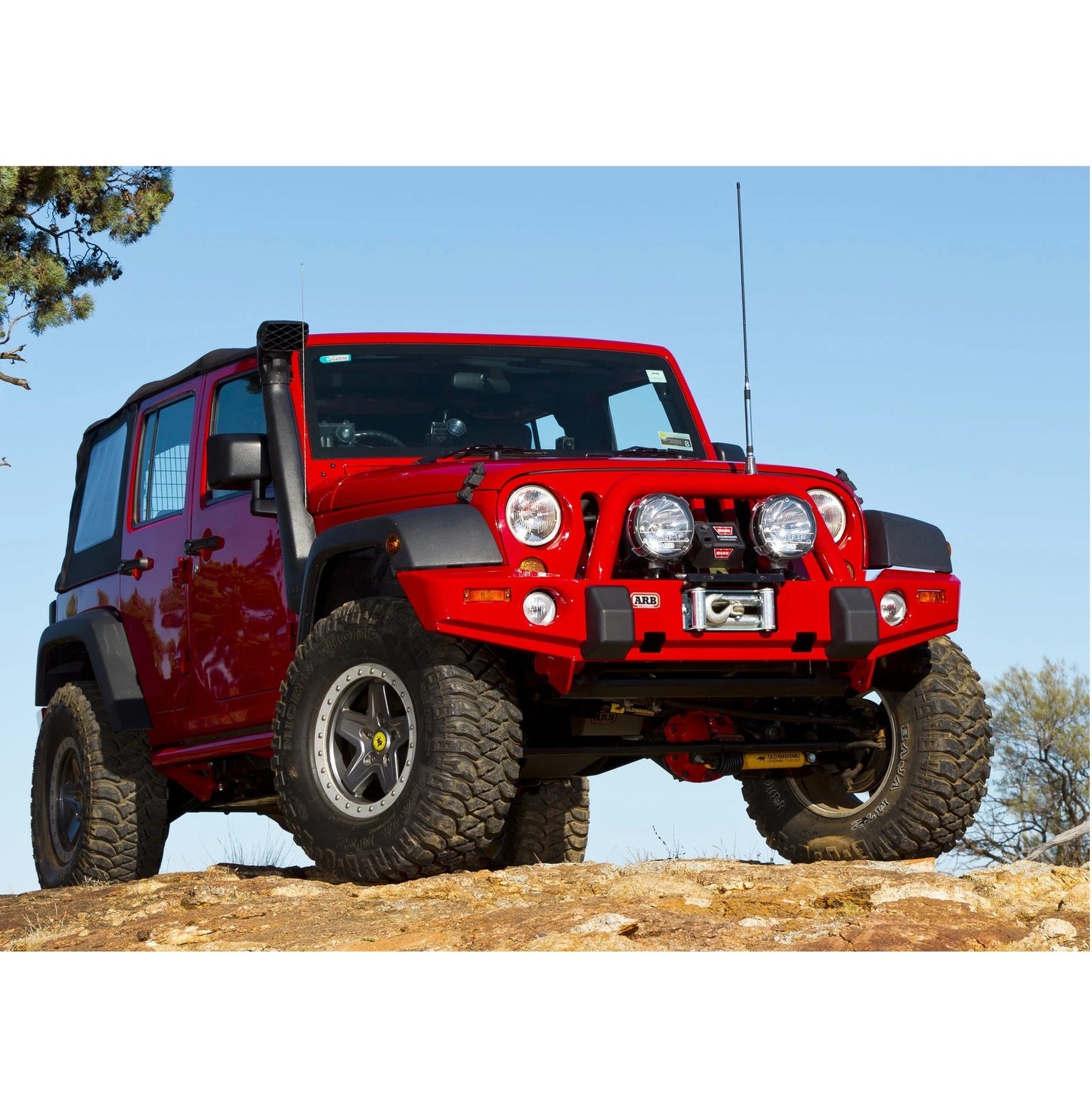 A red Old Man Emu jeep is parked on top of a rock, showcasing its shock absorber performance with the ARB Old Man Emu Front Nitrocharger Sport L Series 60066M for Jeep Wrangler JK.
