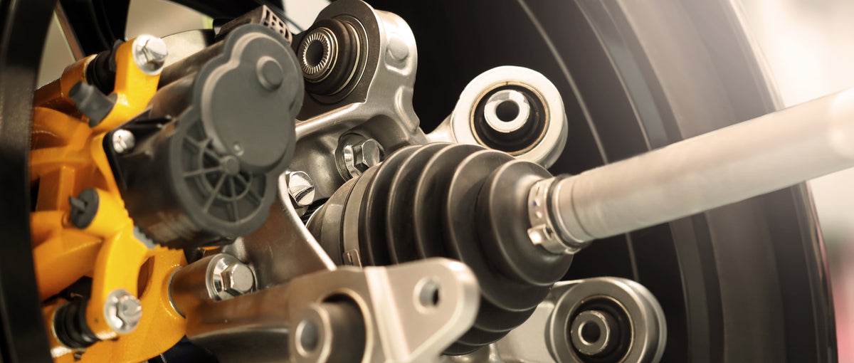 Close-up of vehicle suspension with CV axle, control arms, bushings, and yellow brake caliper