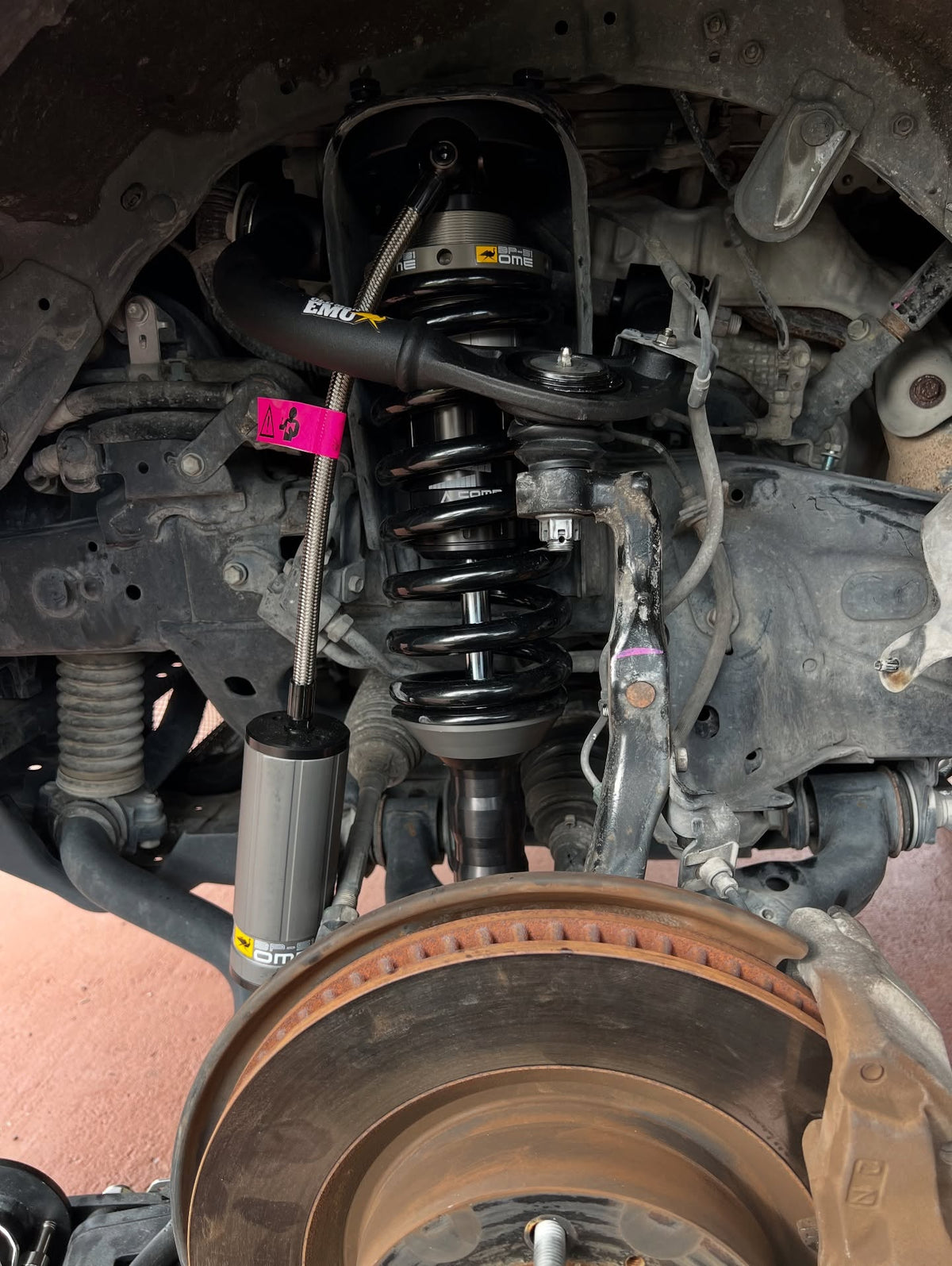 Front suspension with coil spring, shock absorber, control arm, and exposed brake rotor in a wheel well