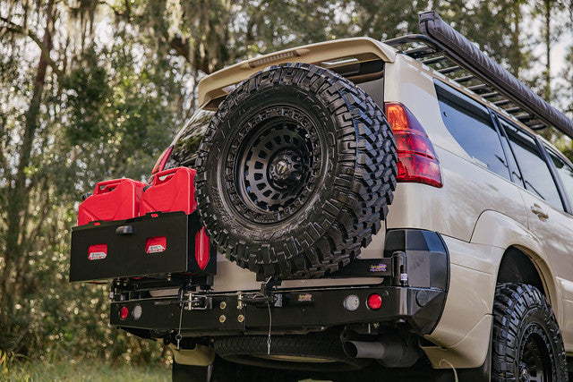 Off road SUV with rear spare tire, steel bumper, swing out carrier, and red fuel cans in a wooded setting