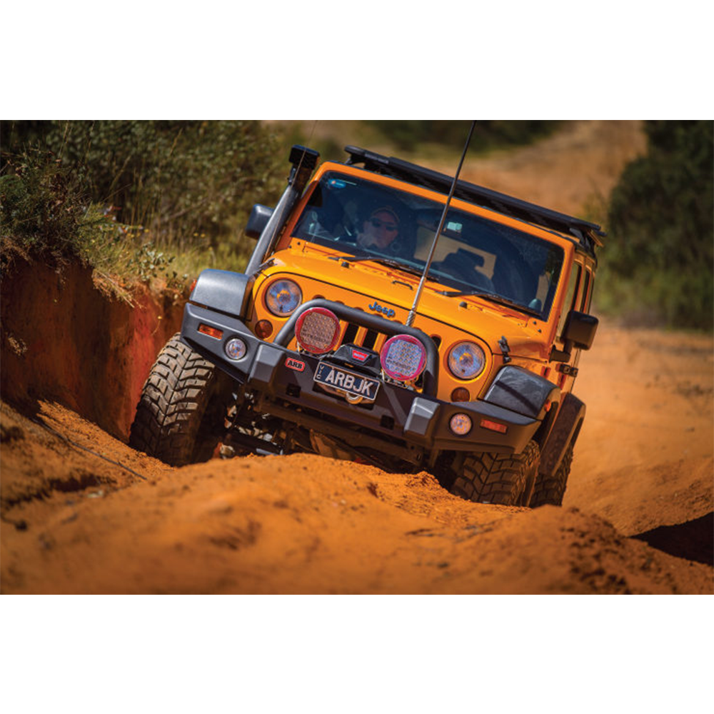 An Old Man Emu orange jeep with excellent shock absorber performance, specifically the ARB Old Man Emu Front Nitrocharger Sport L Series 60066M, is driving down a dirt road.