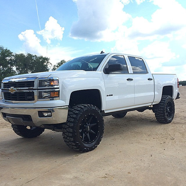 White Chevrolet Silverado pickup with lifted suspension, aggressive off road tires, and black wheels