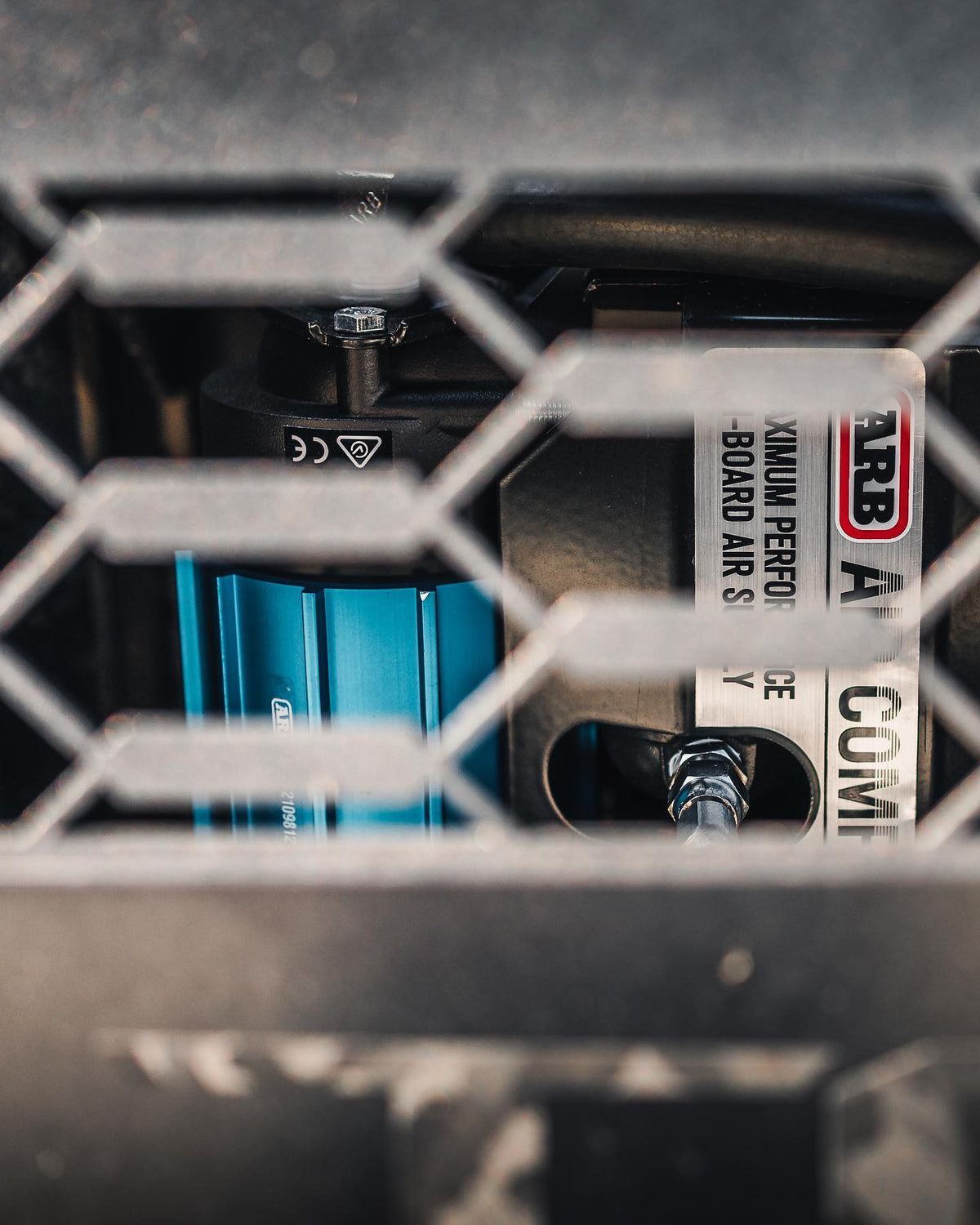 ARB air system components with a blue cylindrical unit viewed through protective mesh in an off-road vehicle.