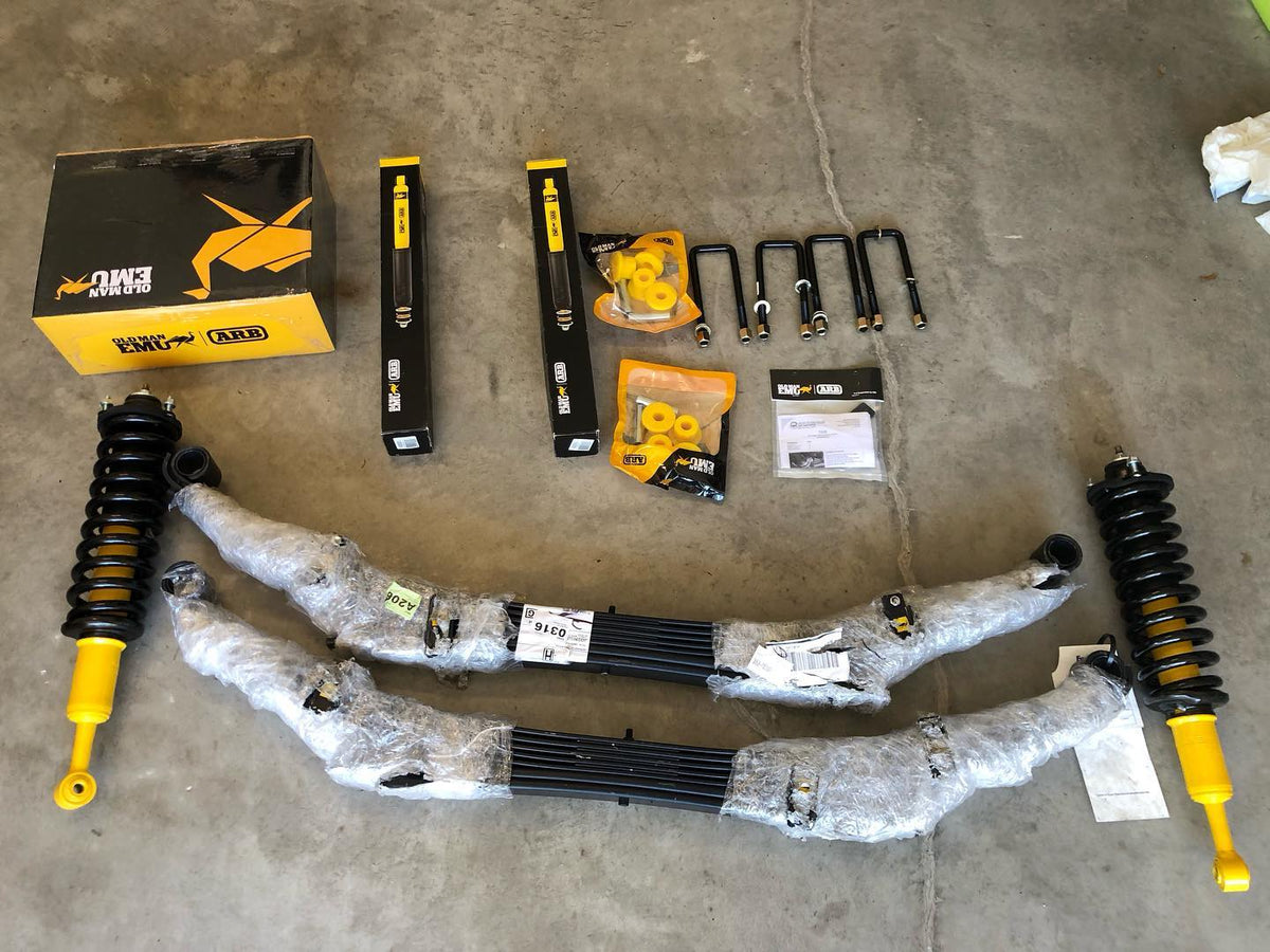 Off-road suspension components with yellow shocks, leaf springs, U-bolts, and mounting hardware on a concrete floor