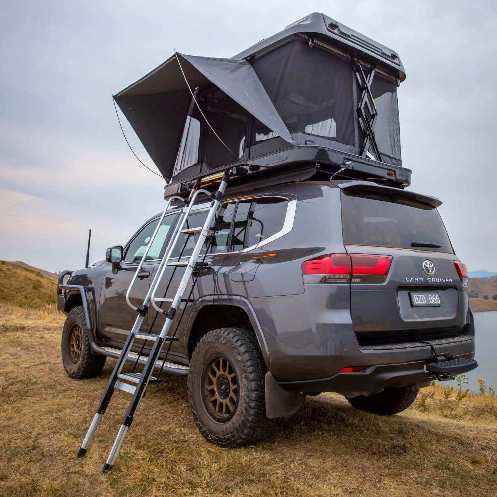 ARB Altitude Hard Shell Electric Rooftop Tent 802500 mounted on 2023 Toyota Land Cruiser with telescoping ladder and rugged off-road tires