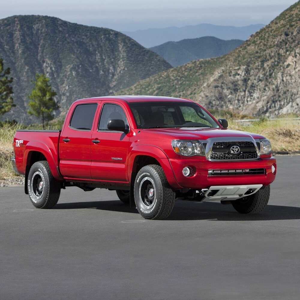 The red Toyota Tacoma, known for its off-road performance and equipped with the powerful Bilstein B8 8112 0.6-2.5 inch Tacoma (05-23) Lift Kit w/ OME Leaf Springs suspension system from Bilstein, is parked in front of magnificent mountains.
