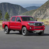 The red Toyota Tacoma, known for its off-road performance and equipped with the powerful Bilstein B8 8112 0.6-2.5 inch Tacoma (05-23) Lift Kit w/ OME Leaf Springs suspension system from Bilstein, is parked in front of magnificent mountains.