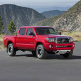 The red Toyota Tacoma, equipped with a Bilstein B8 5100 0-2 inch Tacoma (05-15) Adjustable Leveling Kit, is parked in front of mountains, ready for an off-road experience.