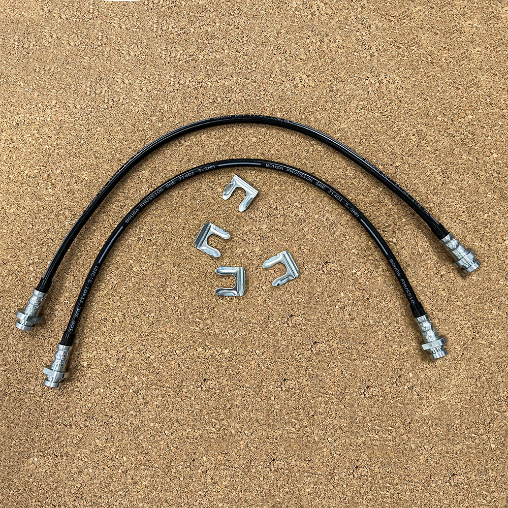 A pair of Mudify Extended Front Brake Lines for Toyota 4Runner 2003-ON, FJ Cruiser 2007-ON, Lexus GX460 & GX470 2003-ON made of black stainless steel on a wooden surface.