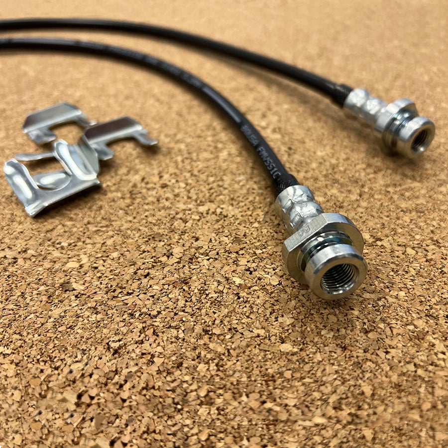 A pair of Mudify Extended Front Brake Lines for Toyota 4Runner 2003-ON, FJ Cruiser 2007-ON, Lexus GX460 & GX470 2003-ON stainless steel brake hoses on a cork surface.