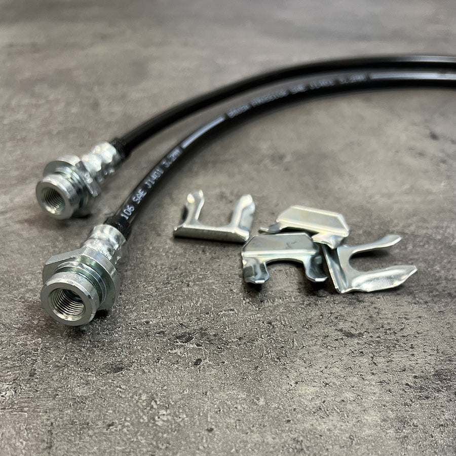 A pair of Mudify Extended Front Brake Lines for Toyota Tacoma 2005-ON supporting axle movement on a concrete surface.