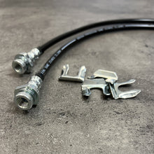 Load image into Gallery viewer, A durable pair of Mudify Extended Rear Brake Lines for Toyota Tacoma 2005-ON allowing for axle movement on a concrete surface.