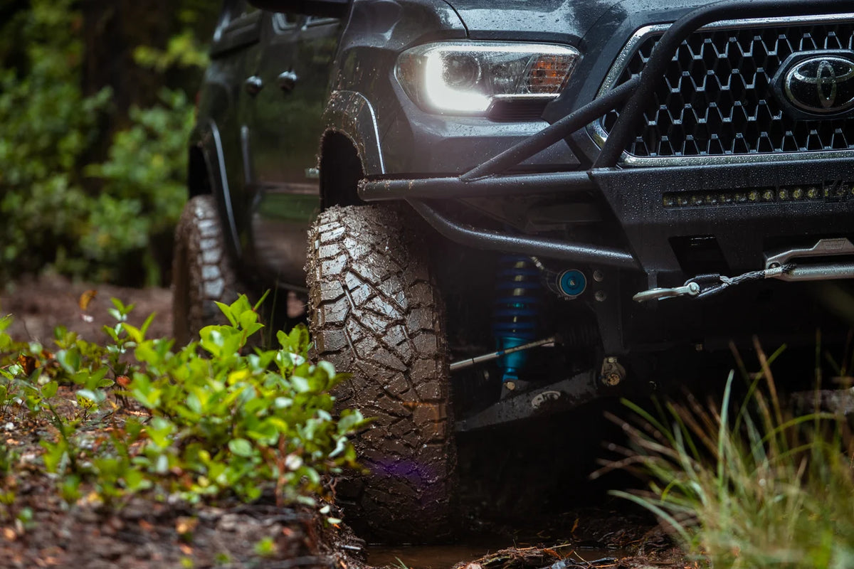 Toyota pickup truck navigating a muddy trail with all-terrain tires and a heavy-duty front bumper