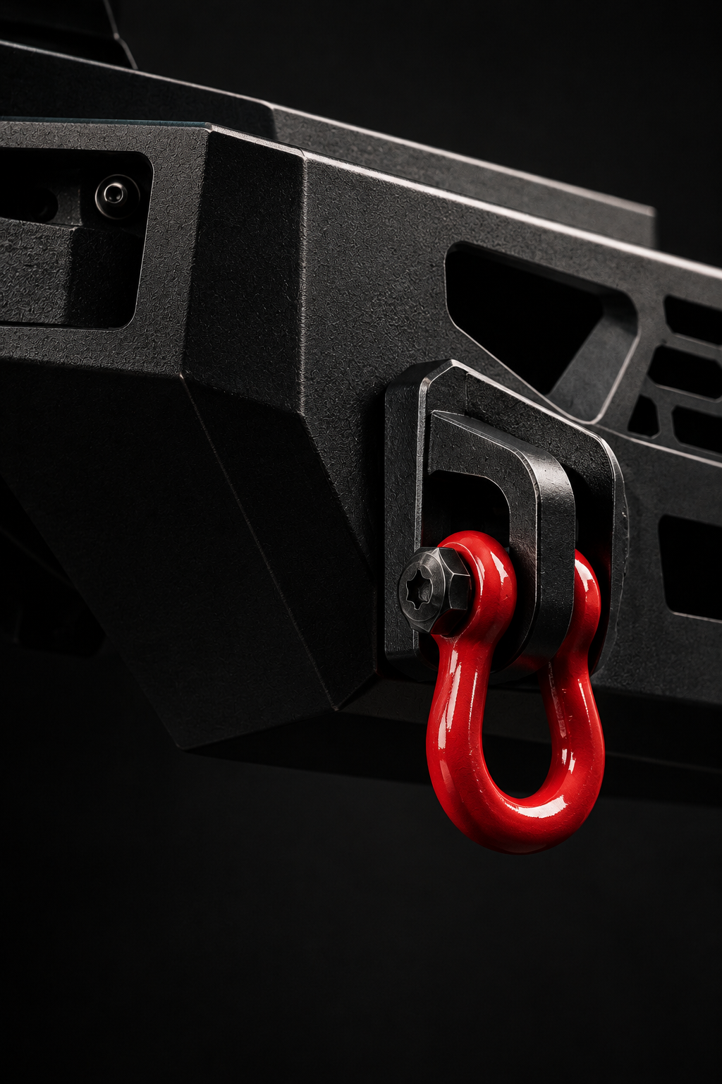 Close-up of a black off-road bumper with a red recovery shackle mounted to a steel bracket