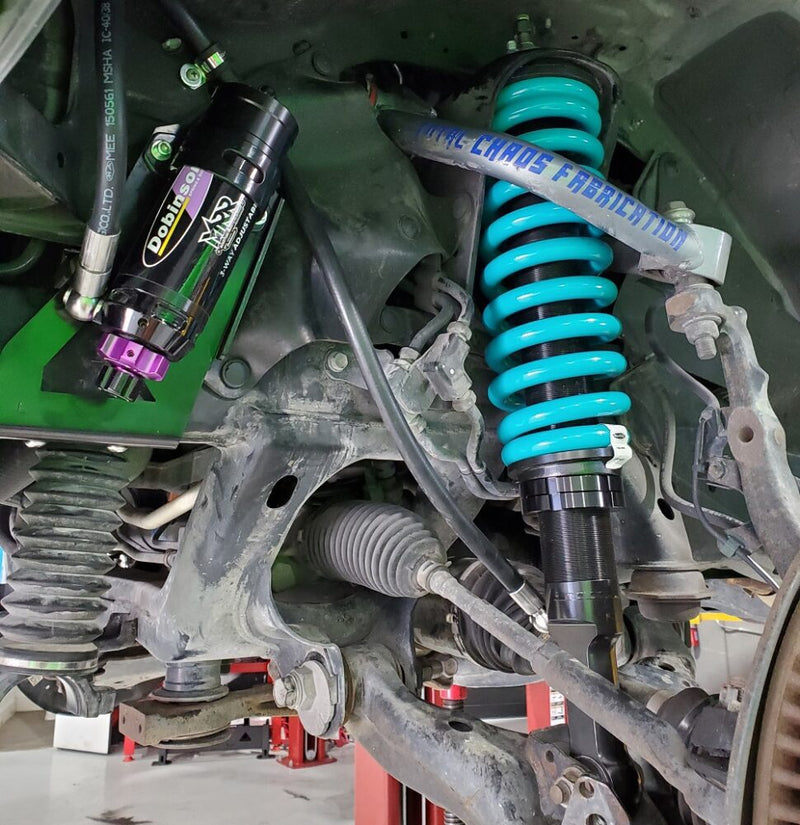 Off-road suspension with turquoise coil springs and adjustable remote reservoir shocks beneath a vehicle