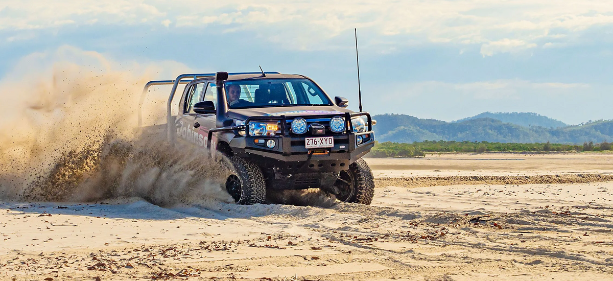 Off-road 4x4 vehicle with bull bar driving through sand and kicking up dust