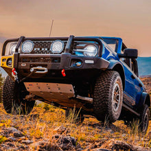 Load image into Gallery viewer, The front end of a blue truck with increased ground clearance on a rocky trail equipped with the Old Man Emu OME 3 inch Lift Kit for Bronco Base, Big Bend, Outer Banks, Wildtrack (21-ON).