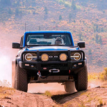 Load image into Gallery viewer, A blue truck with the Old Man Emu 3 inch Lift Kit for Bronco Base, Big Bend, Outer Banks, Wildtrack (21-ON) driving down a dirt road.