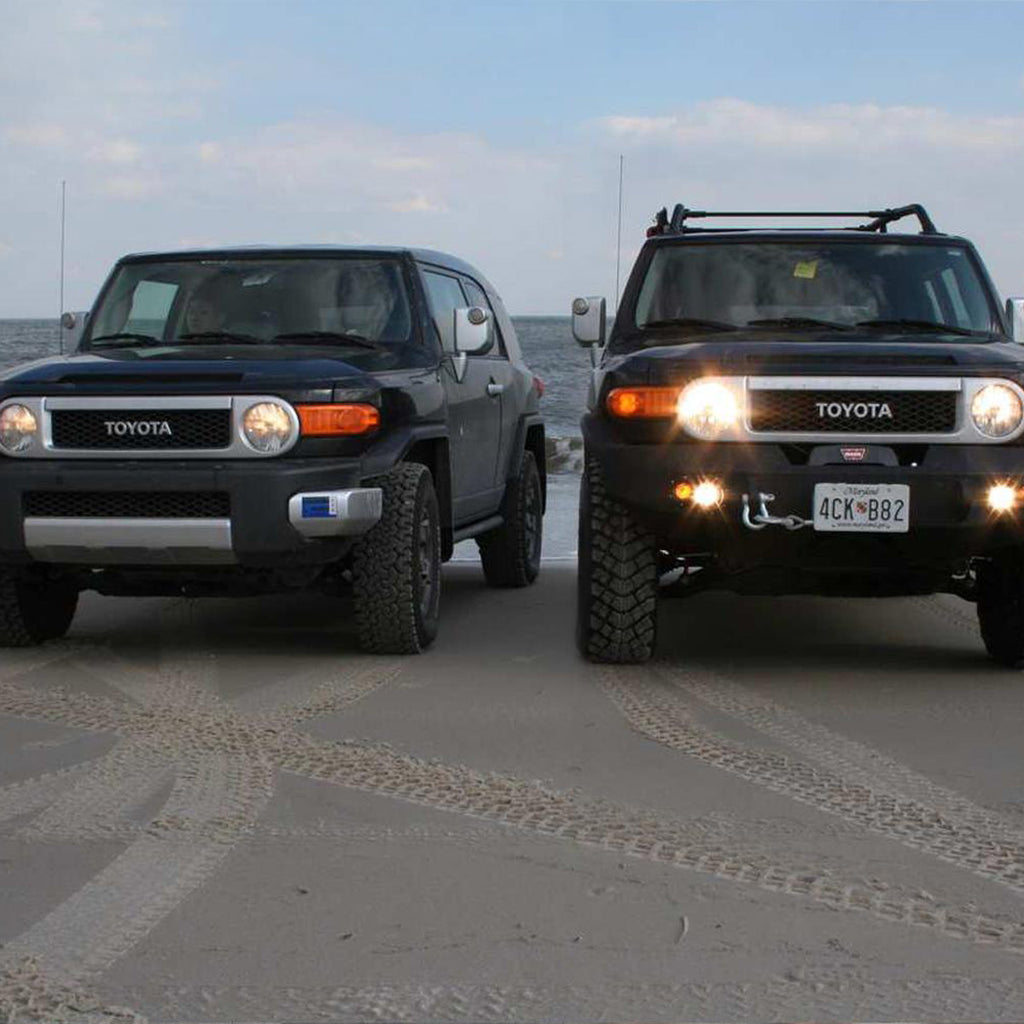 Two Toyota FJ Cruisers parked on the beach, showcasing their impressive ground clearance and equipped with the Old Man Emu OME 3 inch Lift Kit for FJ Cruiser (10-ON) - Front Shocks Assembly.