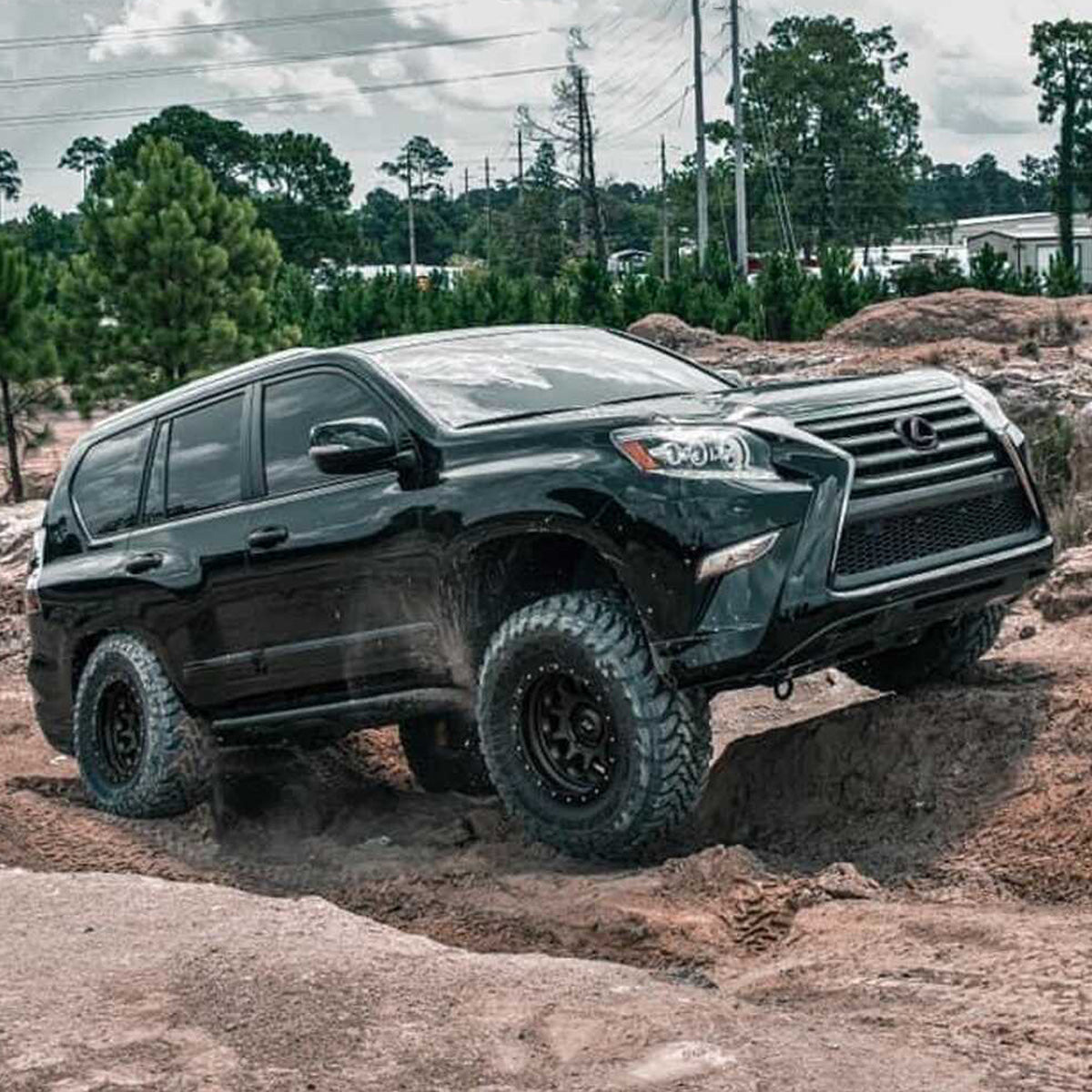 A black Old Man Emu Lexus SUV with impressive ground clearance and a reliable suspension system, confidently navigating through a muddy area.