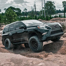 Load image into Gallery viewer, A black Old Man Emu Lexus SUV with impressive ground clearance and a reliable suspension system, confidently navigating through a muddy area.