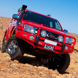 An OME 2.5 - 3 inch Essentials Lift Kit Hilux Vigo (05-15)-equipped red Toyota Tacoma is driving through a desert, showcasing its exceptional ground clearance and advanced suspension system.