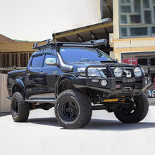 Load image into Gallery viewer, A black pickup truck with an impressive Old Man Emu 2.5 - 3 inch Lift Kit for Hilux Vigo (05-15) suspension system parked in front of a building.