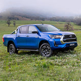 The 2019 Toyota Hilux is parked in a field, showcasing its increased ground clearance thanks to the OME 2.5 - 3 inch Essentials Lift Kit for Hilux Revo, Rocco, SR5 (15-22) by Old Man Emu suspension system and Nitrocharger shocks.
