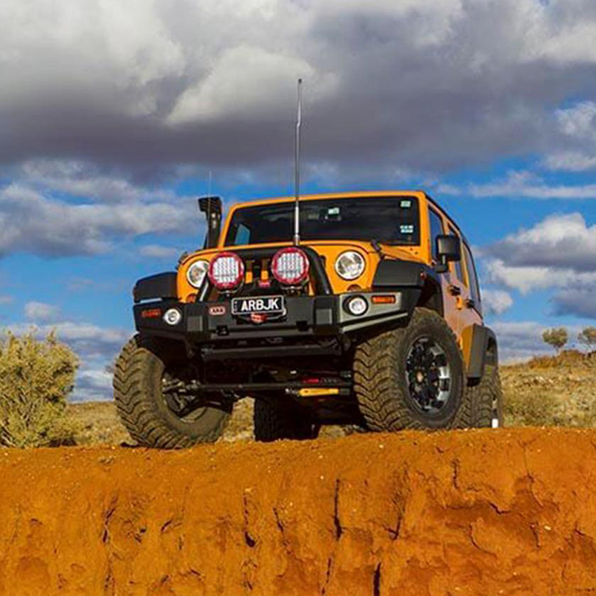 A rugged orange jeep, equipped with an OME 3 inch Lift Kit for Wrangler JK 4 Door (07-18) by Old Man Emu, confidently sits parked on a dusty dirt road. This enhanced setup gives the vehicle increased ground clearance.