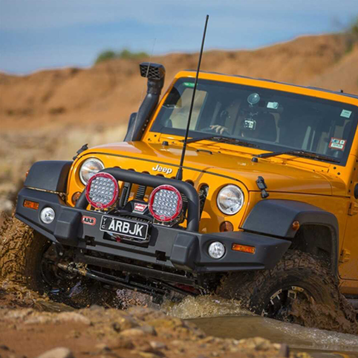An Old Man Emu-outfitted yellow jeep with the OME 4 inch Lift Kit for Wrangler JK 4 Door (07-18) is confidently navigating through a muddy terrain, effortlessly conquering obstacles with its impressive suspension system and exceptional ground clearance.