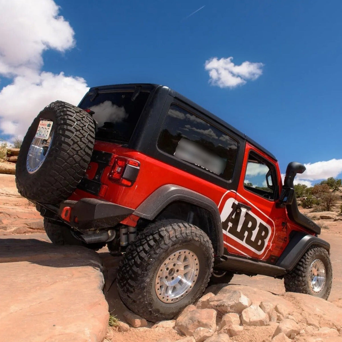 A red Old Man Emu jeep with increased ground clearance is parked on a rock in the desert.