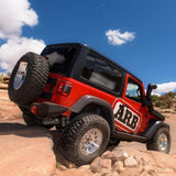 A red Old Man Emu jeep with increased ground clearance is parked on a rock in the desert.