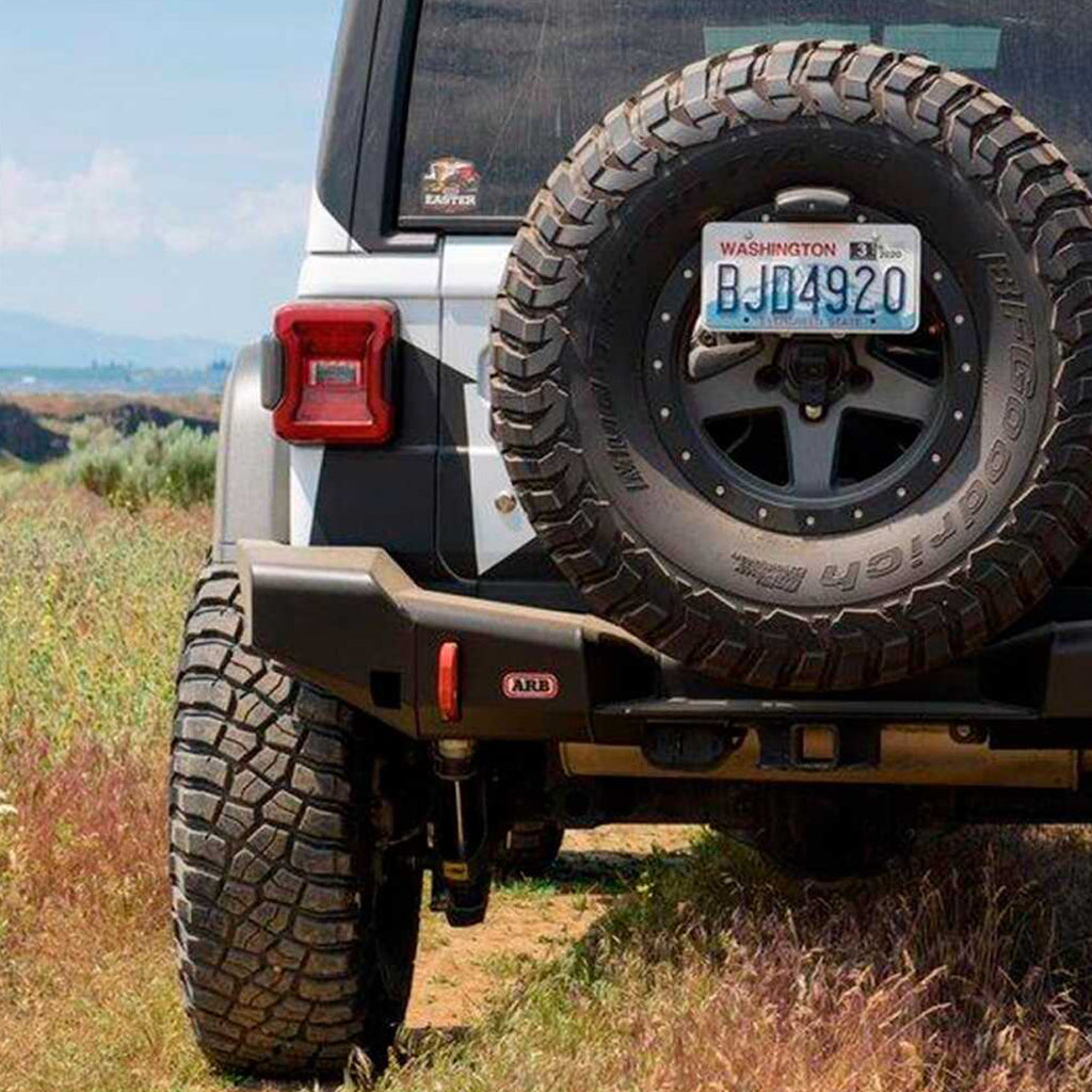 The rear end of an Old Man Emu Jeep Wrangler JL 4 Door (18-23) parked in a field showcasing its impressive ground clearance and Nitrocharger shocks.