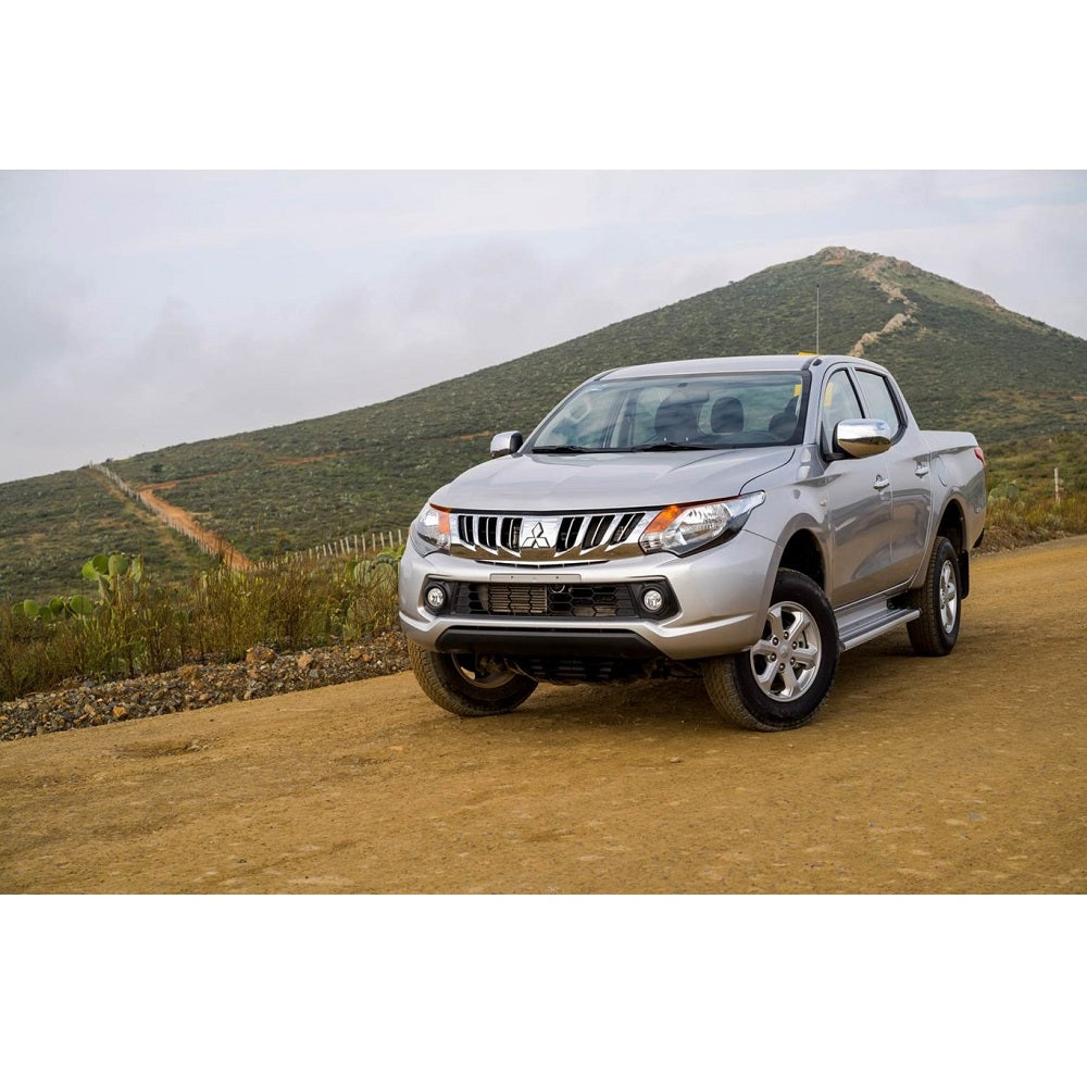 The Mitsubishi Triton, equipped with the Old Man Emu suspension system and Nitrocharger shocks, is parked on a dirt road, showcasing its increased ground clearance.