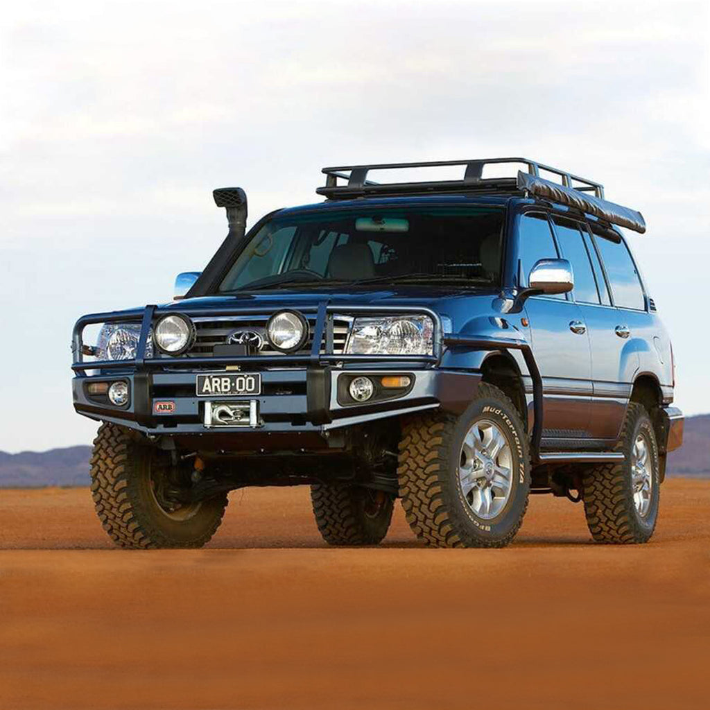 A blue Old Man Emu equipped Toyota Land Cruiser with an impressive ground clearance is parked in the desert.