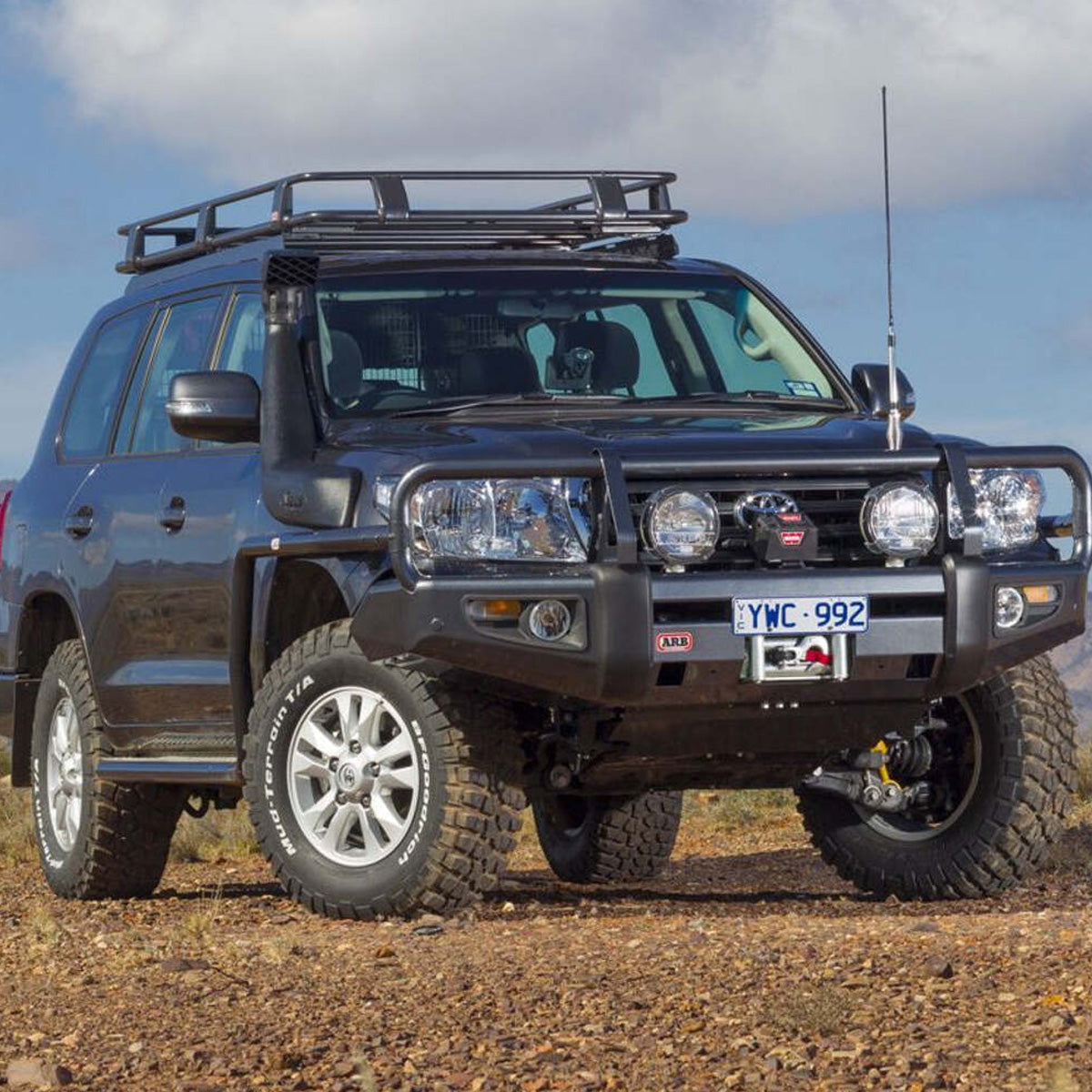 A black Toyota Land Cruiser, equipped with an Old Man Emu OME 1.5 - 2 inch Lift Kit for LandCruiser 200 Series (07-21) suspension system and Nitrocharger shocks, confidently parks on a dirt road, showcasing its impressive ground clearance.