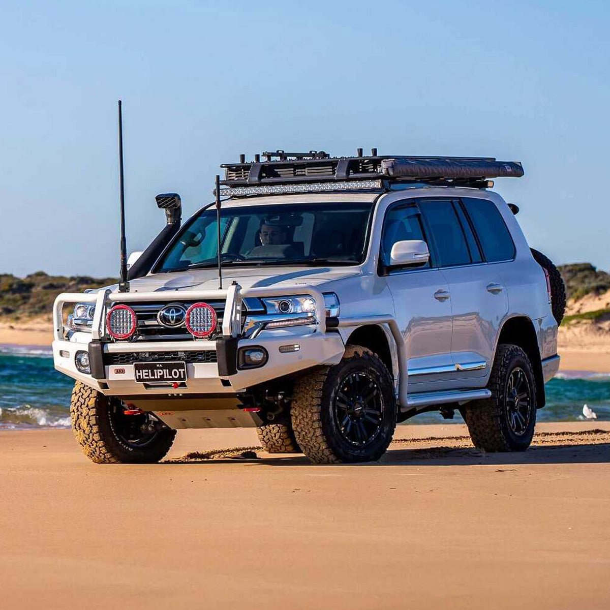 A Toyota Land Cruiser with an OME 1.5 - 2 inch Lift Kit for LandCruiser 200 Series (07-21) by Old Man Emu suspension system and Nitrocharger shocks is parked on the beach, showcasing its exceptional ground clearance.