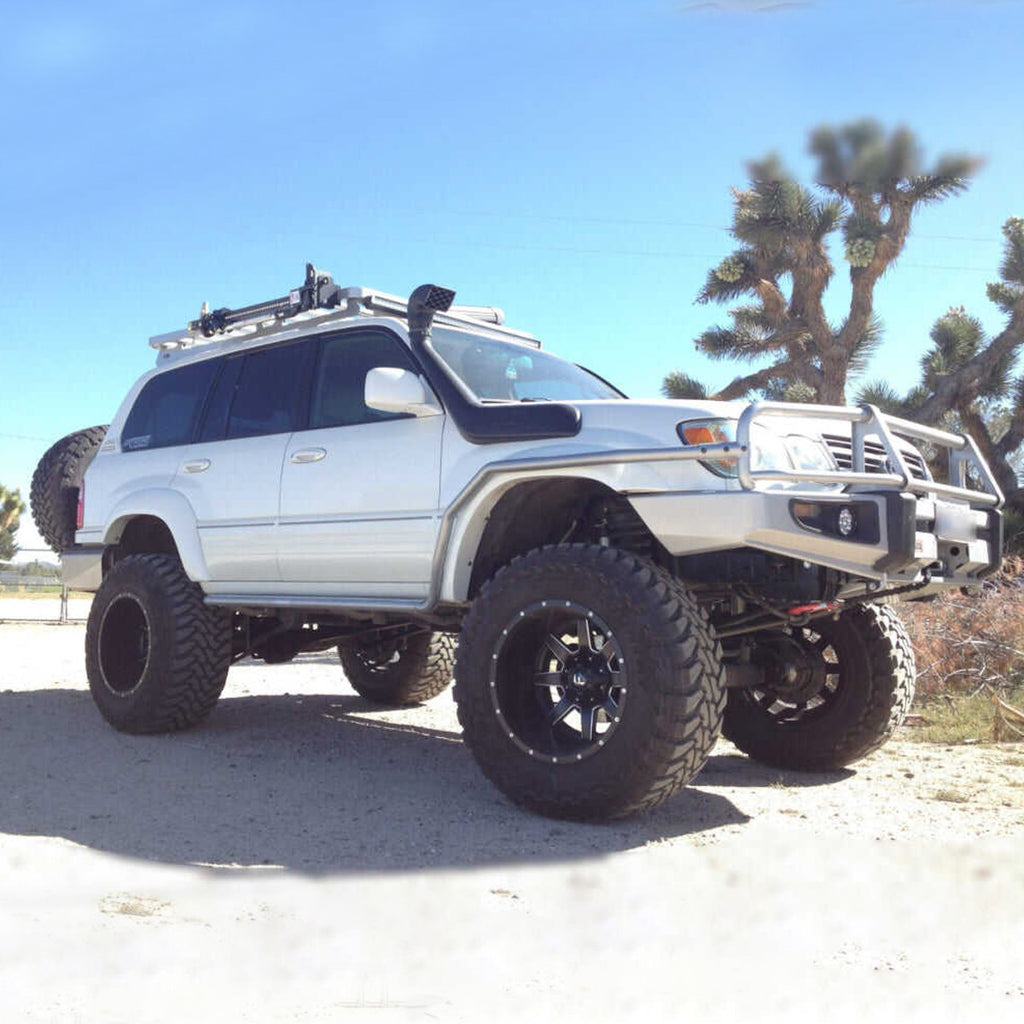 An Old Man Emu-upgraded white Toyota Land Cruiser equipped with the OME 2 inch Lift Kit for LandCruiser 80 & 105 Series (90-07) is parked on a dirt road, showcasing its impressive ground clearance and advanced suspension system.