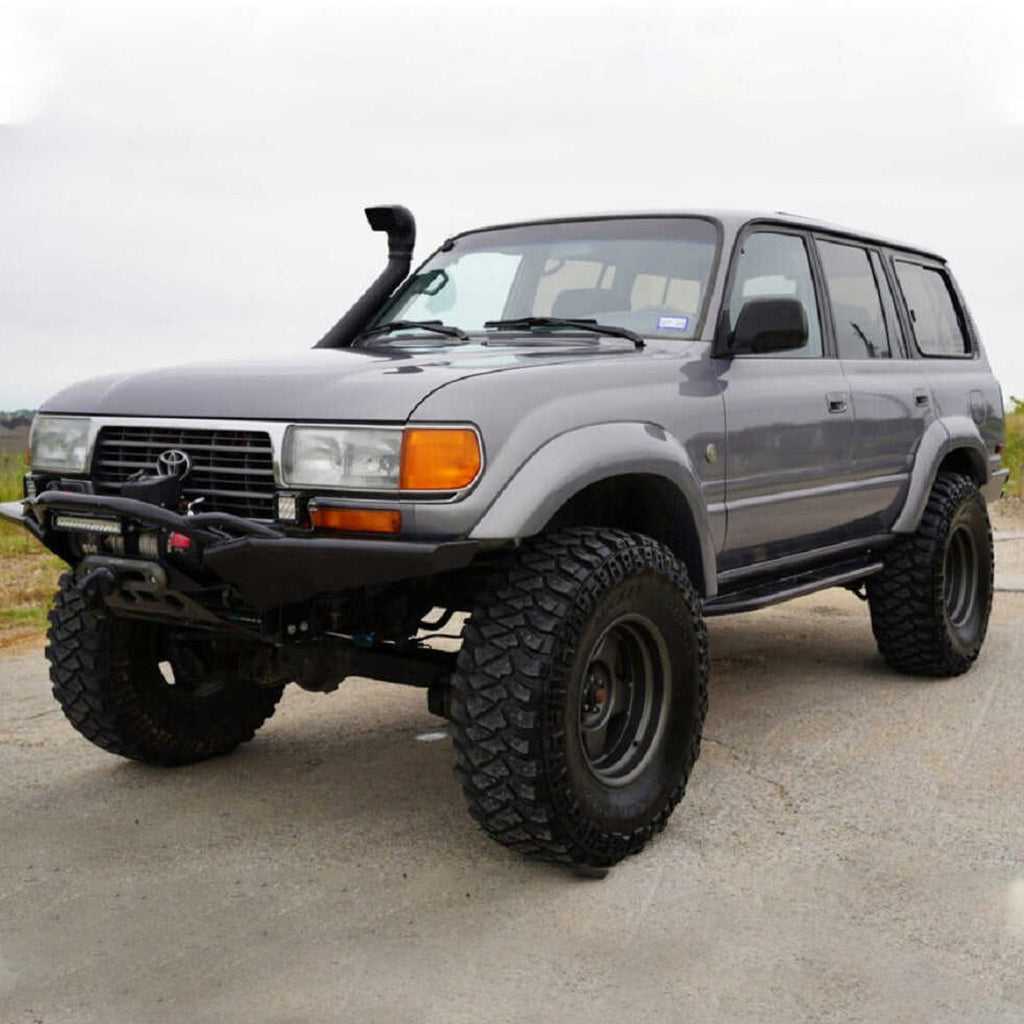 A gray Toyota Land Cruiser with an Old Man Emu 4 inch Lift Kit for LandCruiser 80 & 105 Series (90-07) is parked in a parking lot.