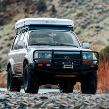 Load image into Gallery viewer, A Toyota Land Cruiser parked on the side of a river, equipped with an Old Man Emu OME 2 inch Lift Kit for Lexus LX450 (96-97) suspension system for increased ground clearance and Nitrocharger shocks.