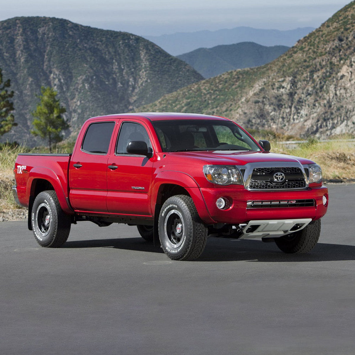 The red Toyota Tacoma, equipped with the OME 2.5 inch Lift Kit for Tacoma (05-15) from Old Man Emu, is parked in front of mountains.
