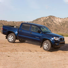 Load image into Gallery viewer, A blue Toyota Tacoma, equipped with the OME 2.5 inch Essentials Lift Kit for Tacoma (05-15) by Old Man Emu, is driving down a dirt road.