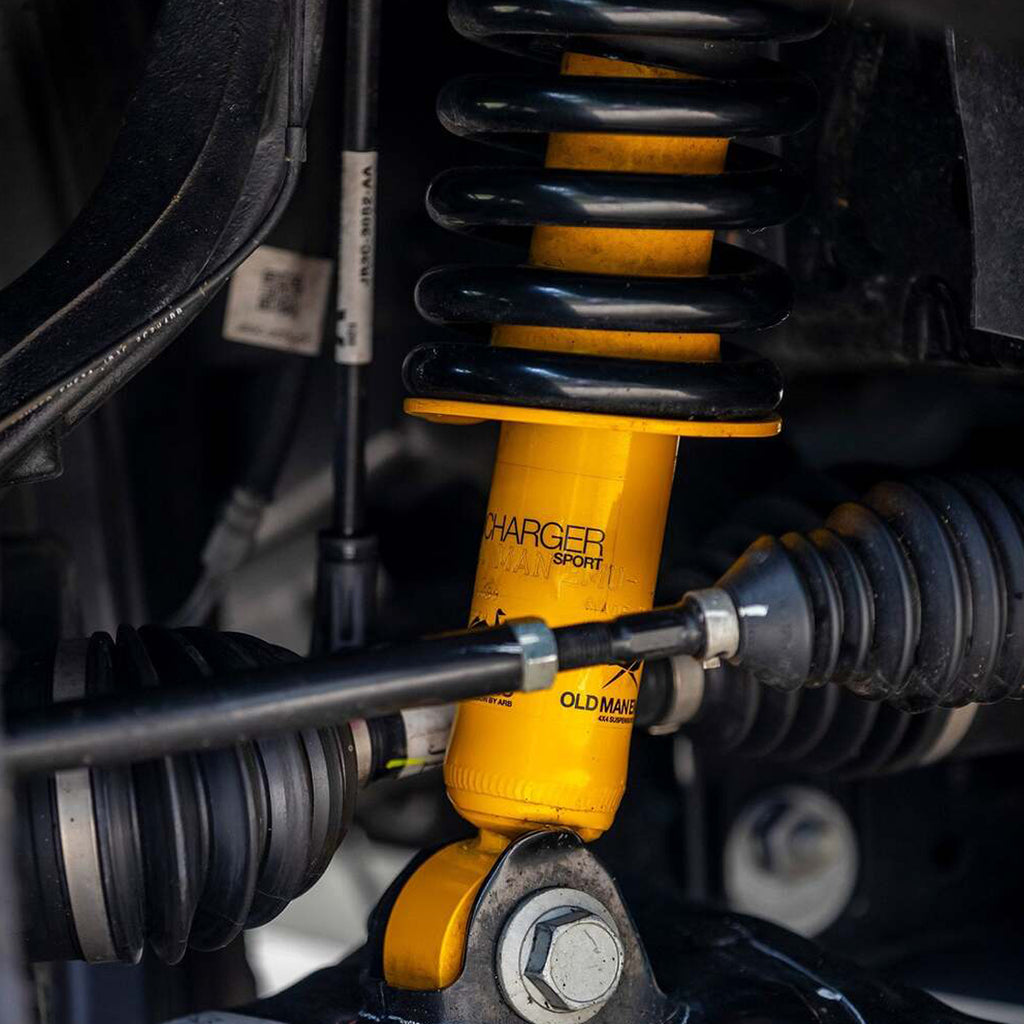 A yellow shock absorber, specifically the OME 2 inch Essentials Lift Kit for Tacoma (05-15) - Front Shocks Assembly by Old Man Emu, is attached to a vehicle. This upgrade, featuring Nitrocharger shocks, provides increased ground clearance for improved off-roading capabilities.