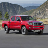 The red Toyota Tacoma with an OME 3 inch Lift Kit for Tacoma (05-15) by Old Man Emu is parked in front of mountains.